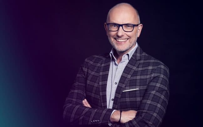 Professionelles Foto von einem Trainer. Er trägt einen Anzug und eine Brille. Er lächelt in die Kamera.